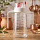 Glass Oil Dispenser Bottle 500ml with Auto-Flip Red Cap, White Side Handle and ml/oz Measurement Scale on Rustic Wooden Kitchen Counter